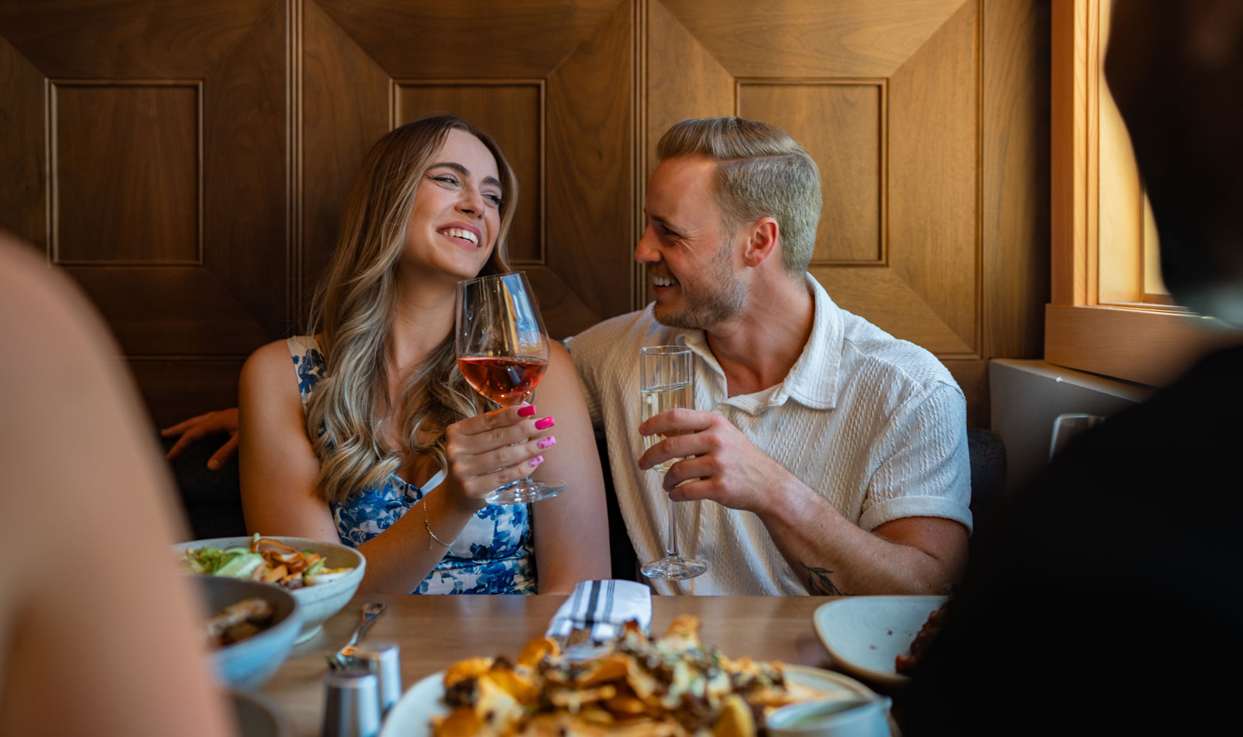 couple sitting at table in a restaurant, holding up drinks and smiling at one another